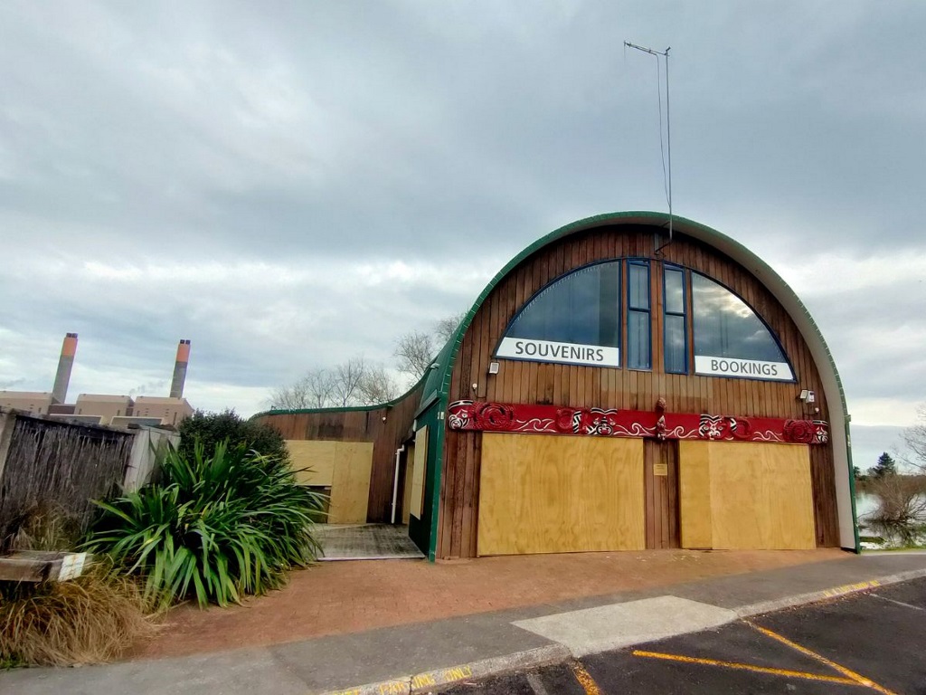 Curved wooden building with boarded-up windows labeled Souvenirs and Bookings under a cloudy sky.