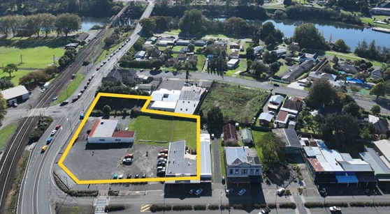 Aerial view of a neighborhood with a large rectangular area outlined in yellow, featuring buildings, a parking lot, and green space. Surrounding roads are busy with traffic, lined with trees and houses, conveying a suburban feel.